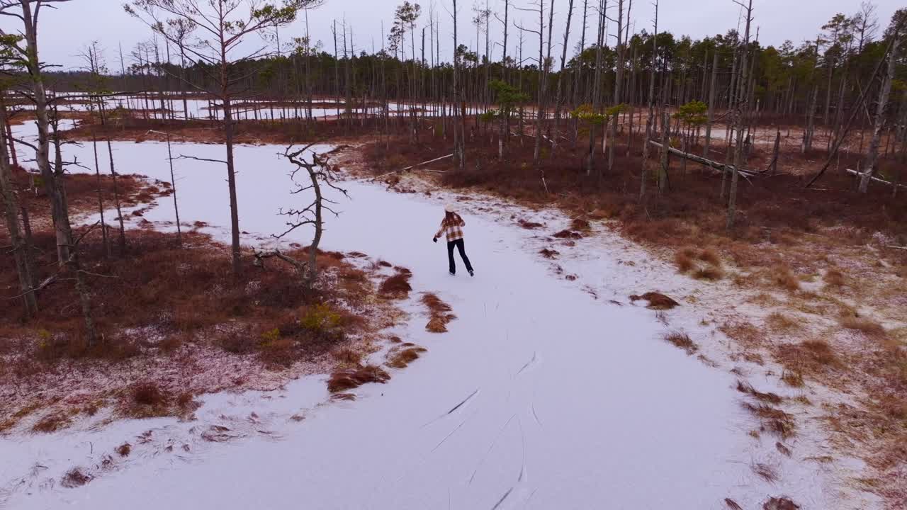 Drone follows woman skating slowly between icy islands in Latvian swamp area