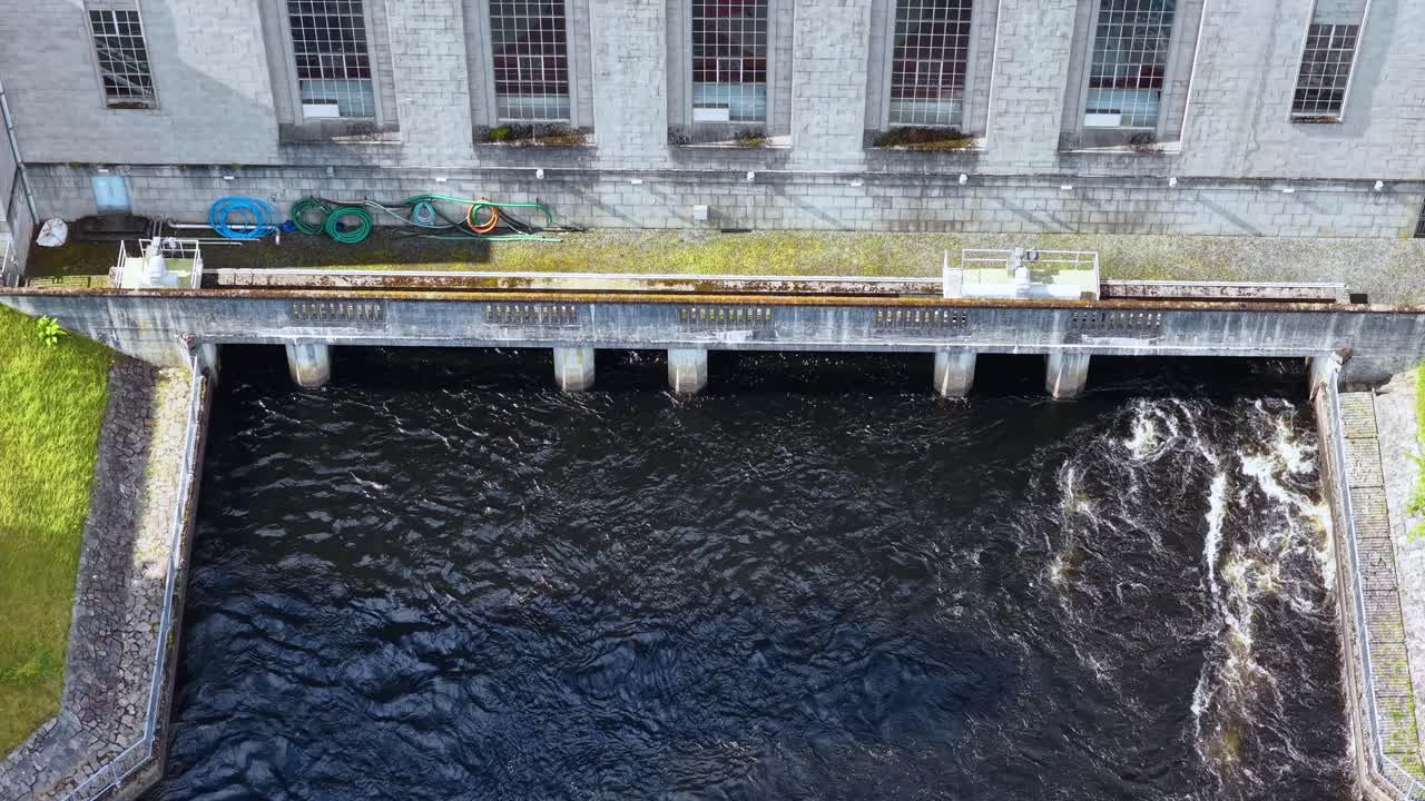 Drone captures hydroelectric power station exterior, river water flow, and dam infrastructure in daylight
