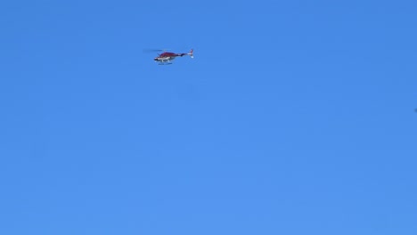 distant view of a private helicopter flying, clear blue sky in background, las americas, tenerife, spain, sunny summer day, handheld tracking shot