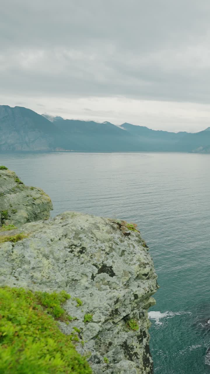 Naturskøn udsigt over en klippefyldt klint, roligt hav og fjerne bjerge