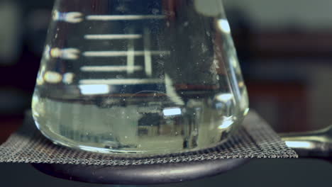 close up erlenmyer flask that is being heated by a bunsen burners no condensation left, heat waves visible in flask, bubbles rapidly forming