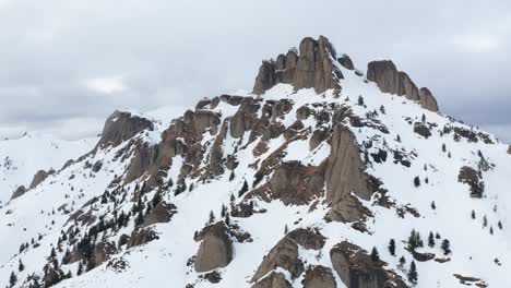 Snow-capped-Ciucas-Mountains-under-overcast-sky,-rocky-peaks,-winter-landscape,-aerial-view