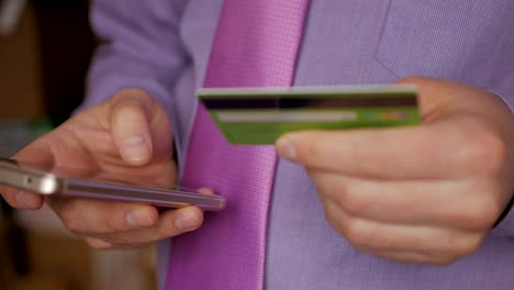 Businessman in a purple shirt making online payment with credit card and smartphone, online shopping, lifestyle technology. Man enters the bank card number into the smart phone. Closeup. Close up.