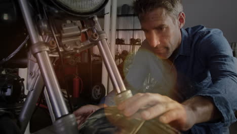 man sanding motorcycle fork in automotive workshop, displaying animated tool icon overlay