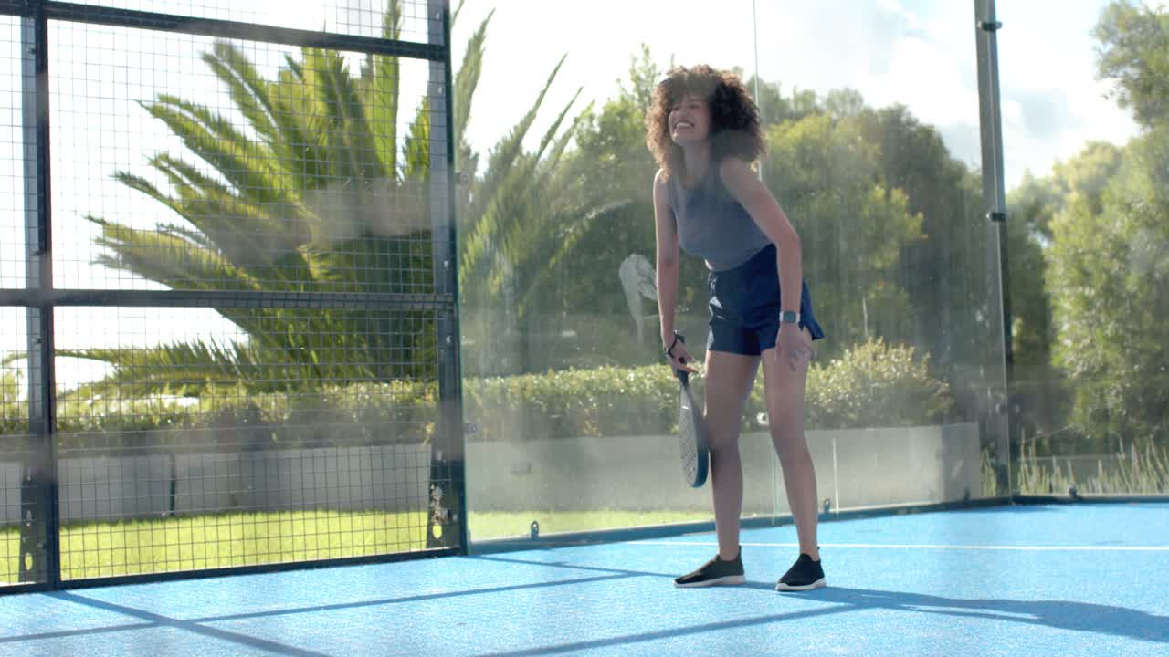 African American woman pausing after rally, standing taller and holding padel racket on blue court
