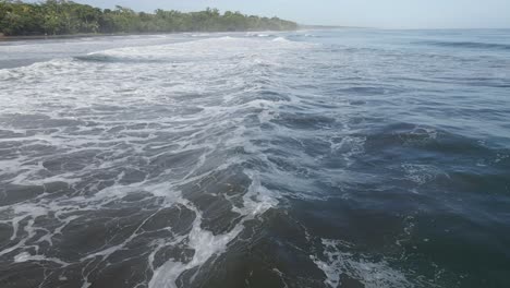 AERIAL---Camera-follows-deep-blue-ocean-waves-into-island-with-green-forest-jungle