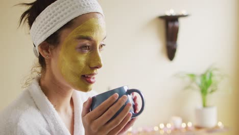 mujer biracial relajada con máscara facial bebiendo café