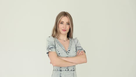 a young woman with blonde hair and a denim dress standing with crossed arms against a white background