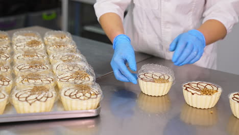sweet creamy desserts packaging. worker's hands in latex gloves put the lids on individual plastic boxes of cake. close up.