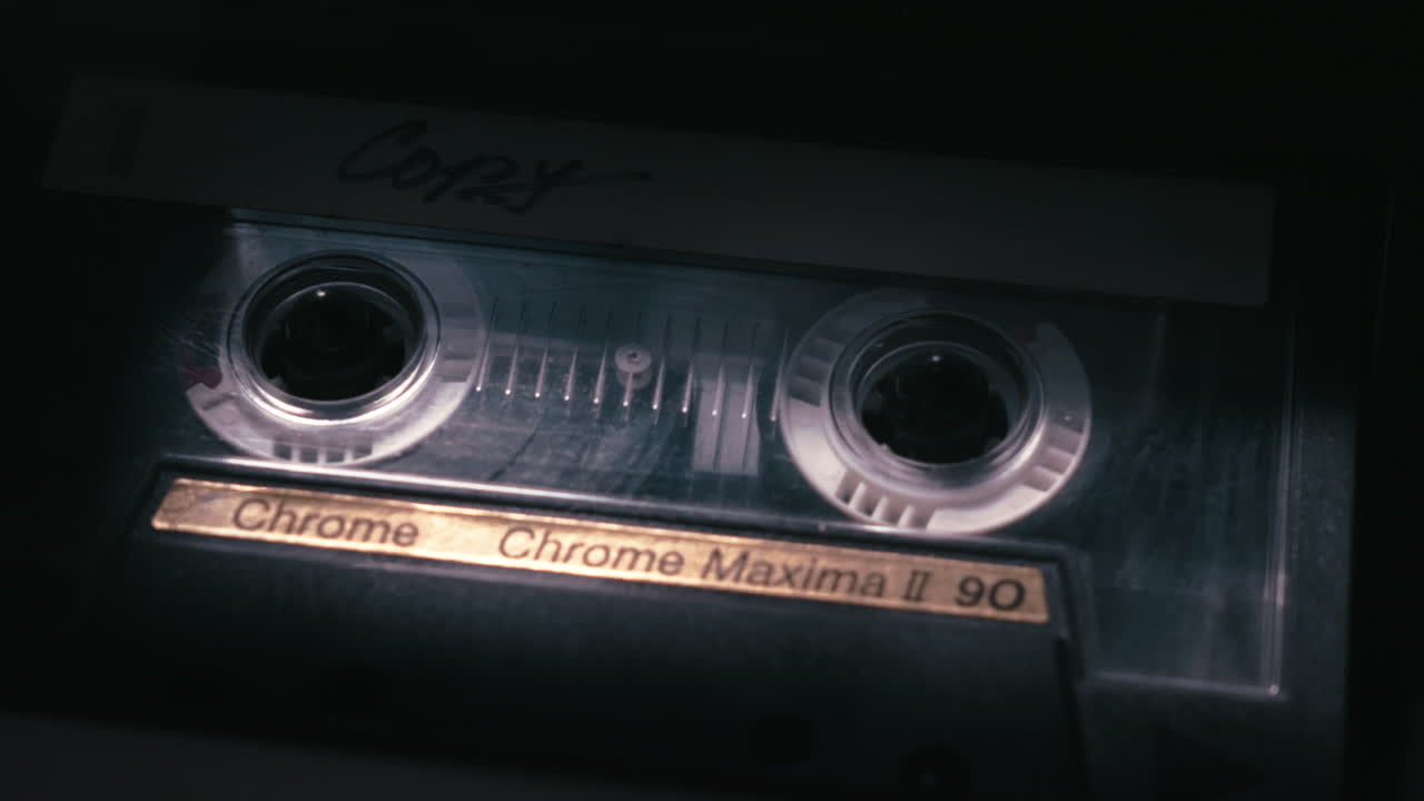 Primo piano di una cassetta analogica che gira in una scena scura, atmosfera da film poliziesco, indagine di polizia, registrazione di dichiarazioni di testimoni.