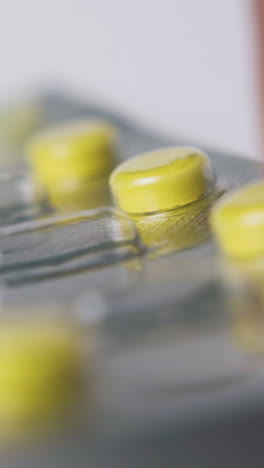 person shows silver blister with bright yellow pills on white background extreme close view