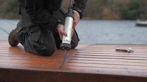 young carpenter sealing roof planking of boat cabin with sealant gun in bleak weather