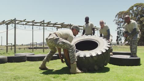 fit caucasian male soldier flipping tractor tyre, with diverse group at army obstacle course