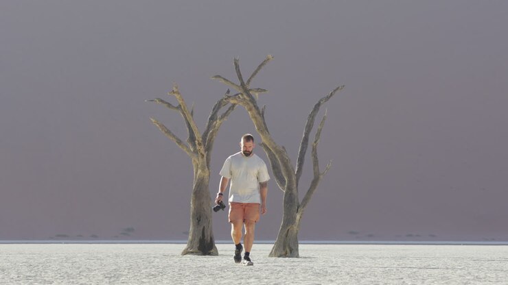 Lone Traveler With Camera On Hand Walking In The Salt Pan At Sossusvlei In Namib-Naukluft National Park