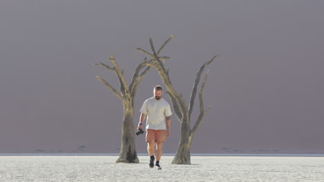 viajero solitario con cámara a mano caminando en la salina en sossusvlei en el parque nacional namib-naukluft