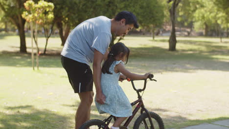 happy asian man teaching his little daughter to ride bike