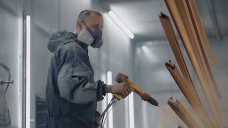 a man in a respirator is painting metal with a powder method. production of steel and metal structures. painting shop. the painter works with a spray gun paint is applied