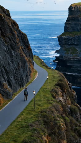 person walks along a dramatic coastal cliff path overlooking the ocean