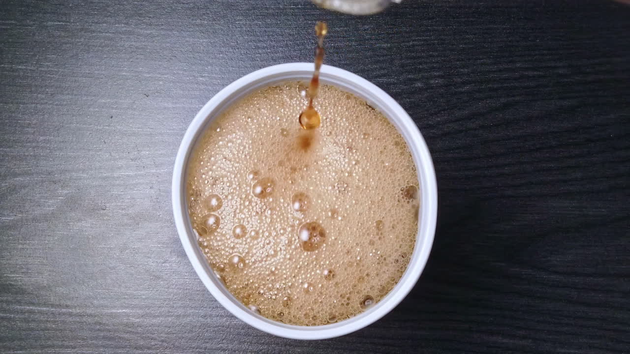 Video al rallentatore dall'alto di cola che viene versata in un bicchiere di plastica bianca su un tavolo di legno in cucina