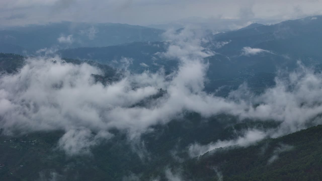 Aerial drone shot of scattered sunbeams illuminating cloud-covered hills.
