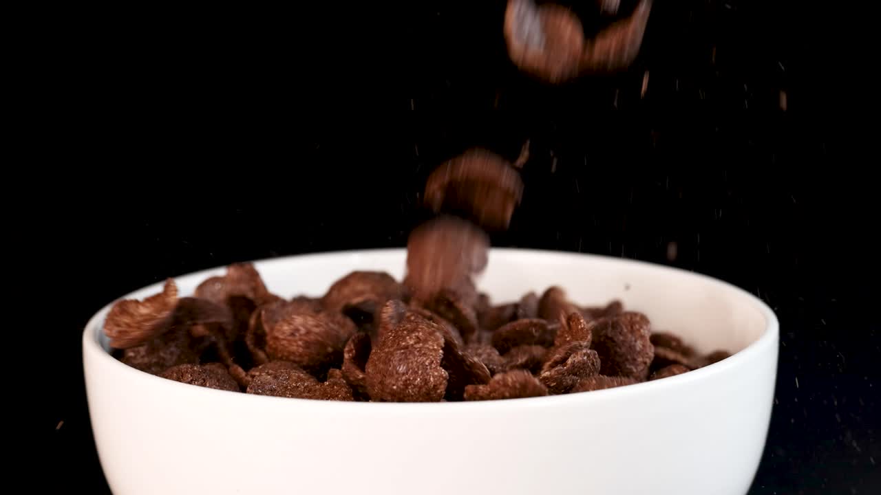 Chocolate cereal pieces cascade into a white bowl against a black background, captured in a smooth, continuous motion