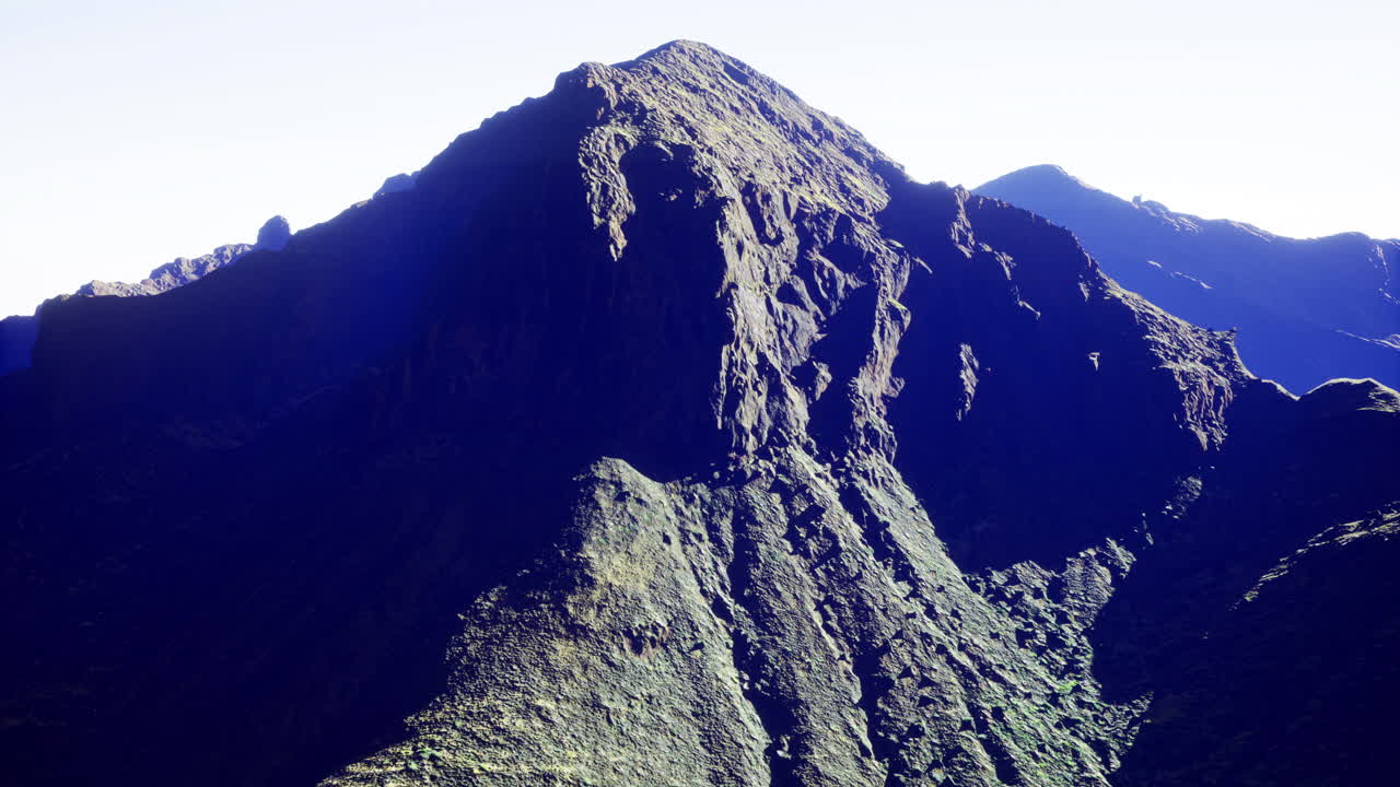 Majestic mountain peak rises above rugged terrain in bright daylight