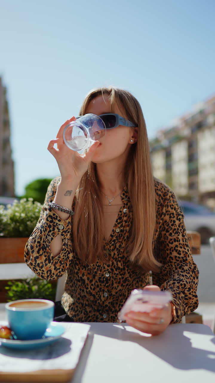 mujer bebiendo agua y usando el teléfono en un café