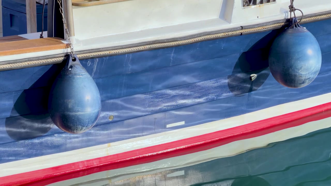 Close-up shot of a blue boat hull with round fenders floating in sunny Mediterranean water
