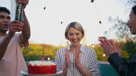 birthday girl blowing cake candles on rooftop party closeup. friends clapping