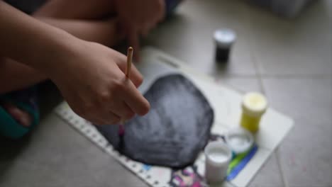 close up of girl painting in natural light. the scene is set in a well-lit indoor environment, where the focus is on the girl's hand holding a paintbrush as she applies paint to a sheet of paper