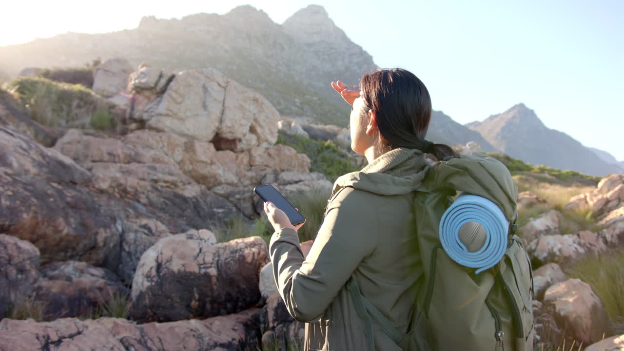 Hiking in mountains, woman with backpack holding smartphone and looking ahead