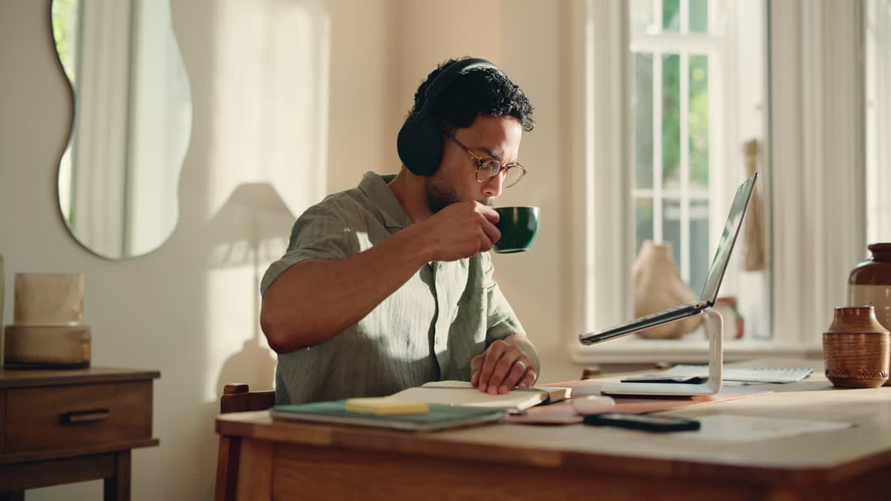 Young Man Working on Laptop and Taking Notes at Home
