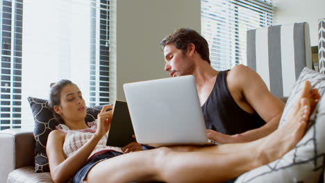 Man-using-laptop-and-woman-reading-a-book-in-living-room-4k