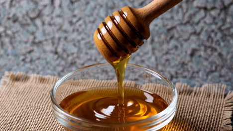 honey pouring from wooden dipper into glass bowl
