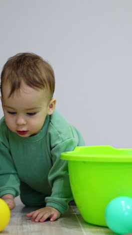 cute baby boy crawls for his ball around the washbowl. black cat is watching the kid and camera. vertical video