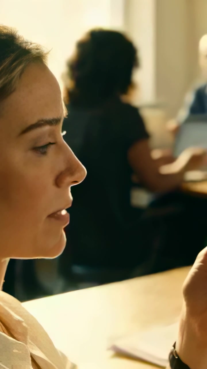 Vertical video: Talking woman in blouse showing phone to coworker while on call at desk, copy space