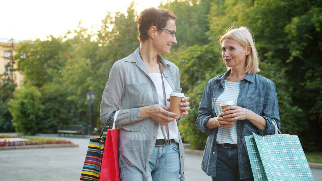Two women friends talking and enjoying coffee in the park while shopping