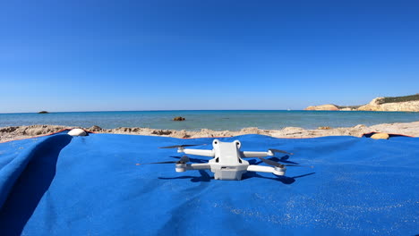 A-stationary-drone-starts-spinning-its-propellers-rapidly-on-a-Greek-beach-in-summer