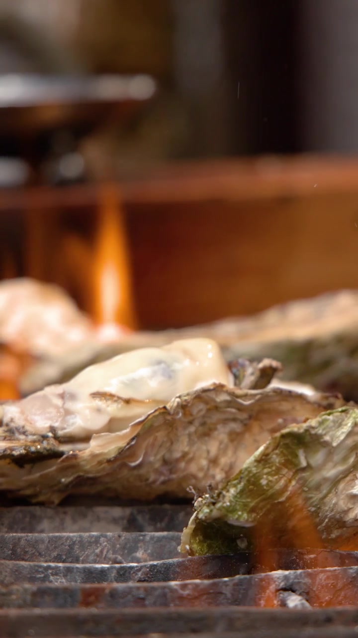 Close-up shot of a chef grilling fresh oysters on an open fire at a market.