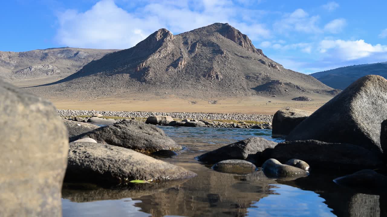 In an untouched Mongolian valley, a rugged mountain's reflection shimmers on a clear river. A tranquil and picturesque scene of the remote autumn wilderness