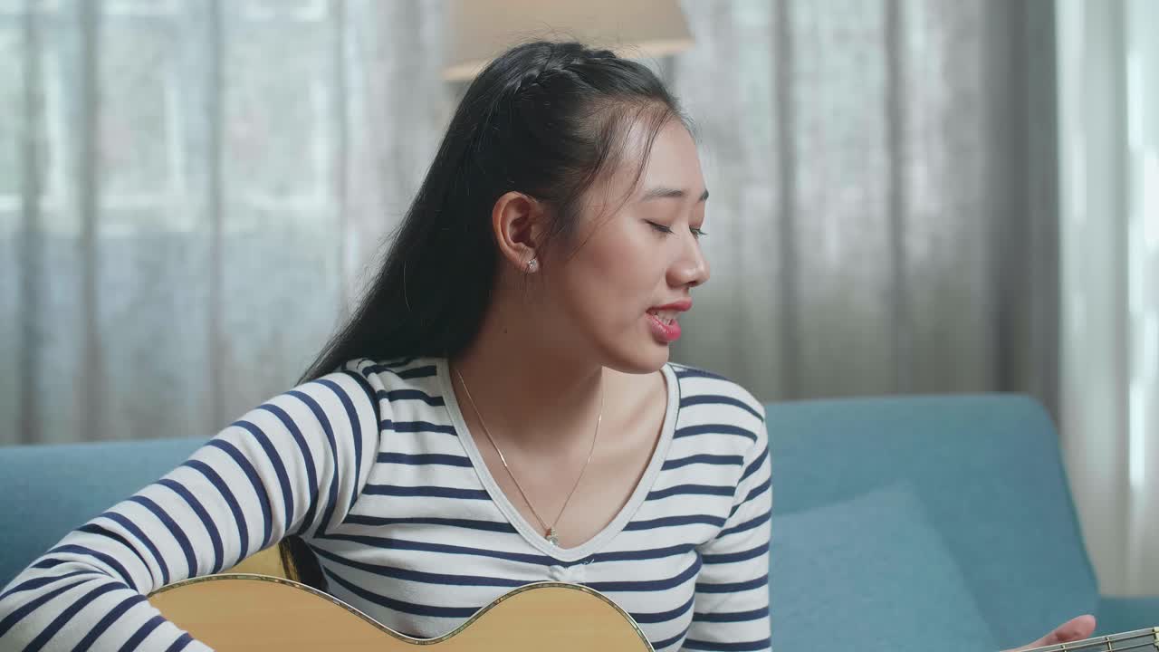 여성이 집에서 노래하고 어쿠스틱 기타를 연주하고 있습니다.