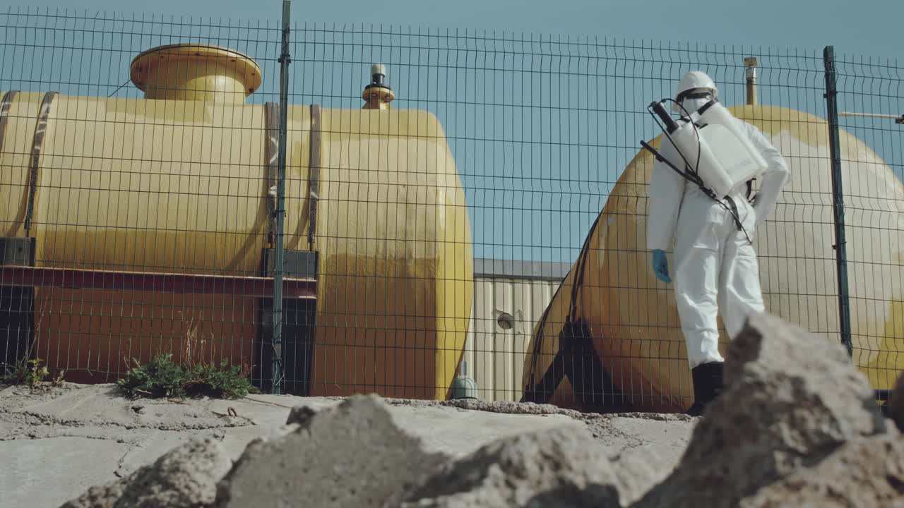 Ecologo che spruzza una recinzione lungo un gasdotto indossando indumenti protettivi