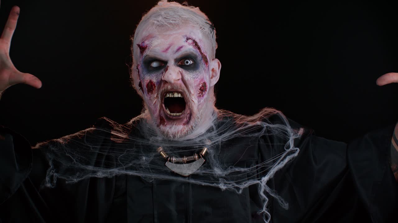 Scary wounded Halloween zombie undead beast man making faces, looks at camera and smiles terribly