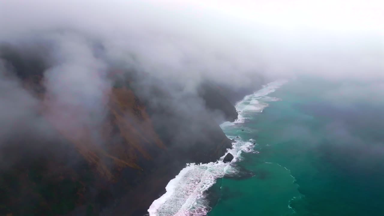 Waves crashing boulder rocks rugged coastline black sand USAL Beach Campground Lost Coast Trail California aerial drone fog mist rain cloudy layers mountainside morning Pacific Ocean backwards motion