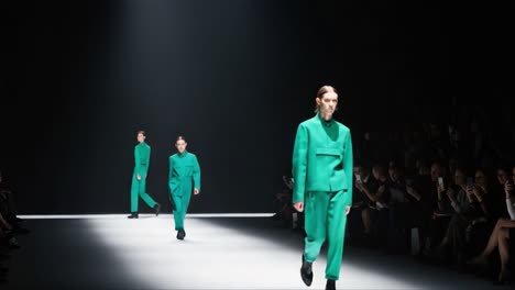a captivating fashion showcase: two models grace the runway in striking green attire under dramatic lighting, embodying contemporary style and elegance