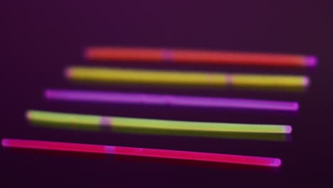 Animation-of-five-colorful-neon-glow-sticks-over-black-background