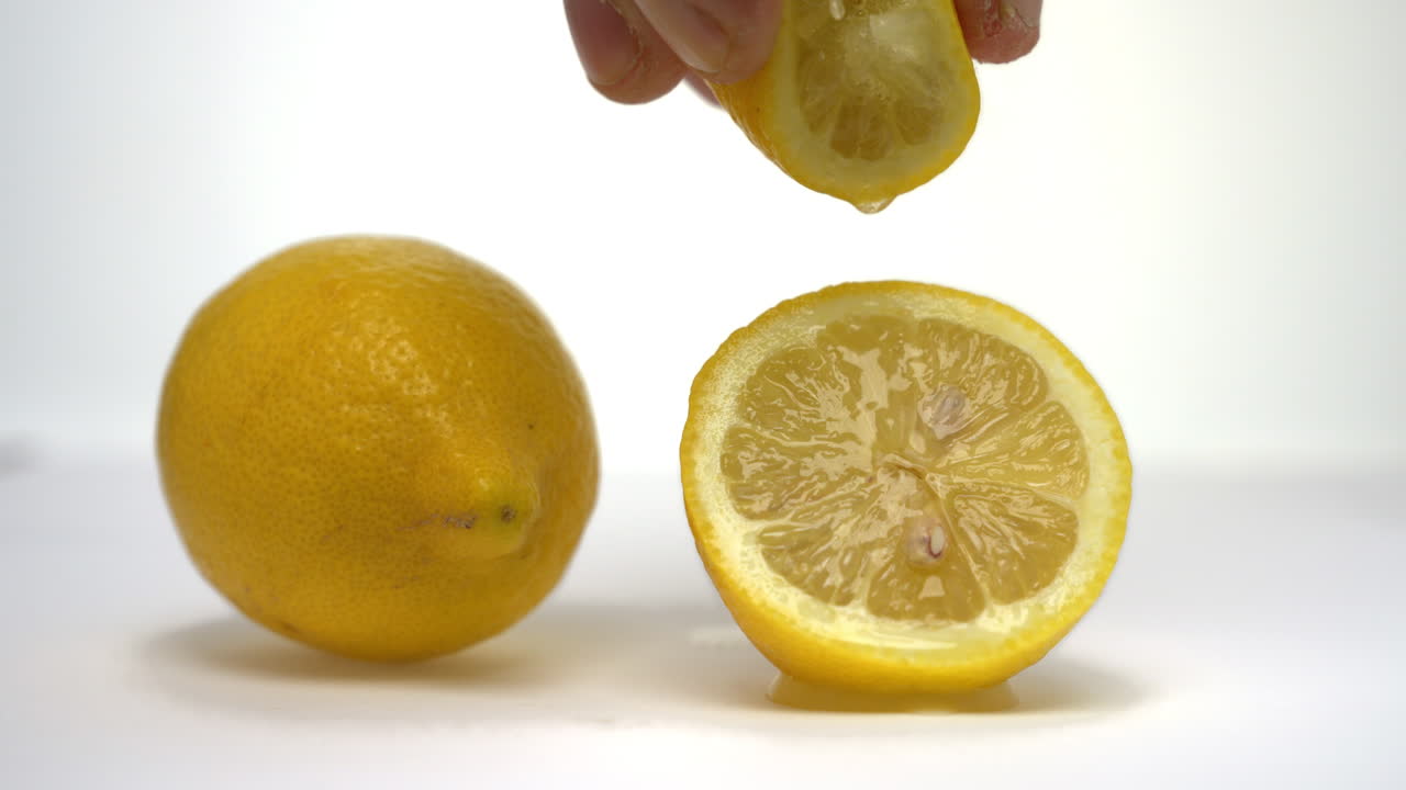 Video orizzontale al rallentatore di una mano che sprema metà limone sopra un'altra metà affettata appoggiata su una superficie, con un limone intero posizionato accanto