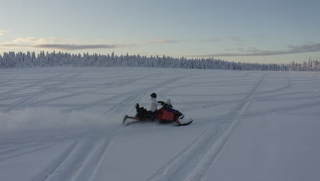 aerial drone shot following a snowmobiler with speed in deep snow in the cold winter landscape of sweden