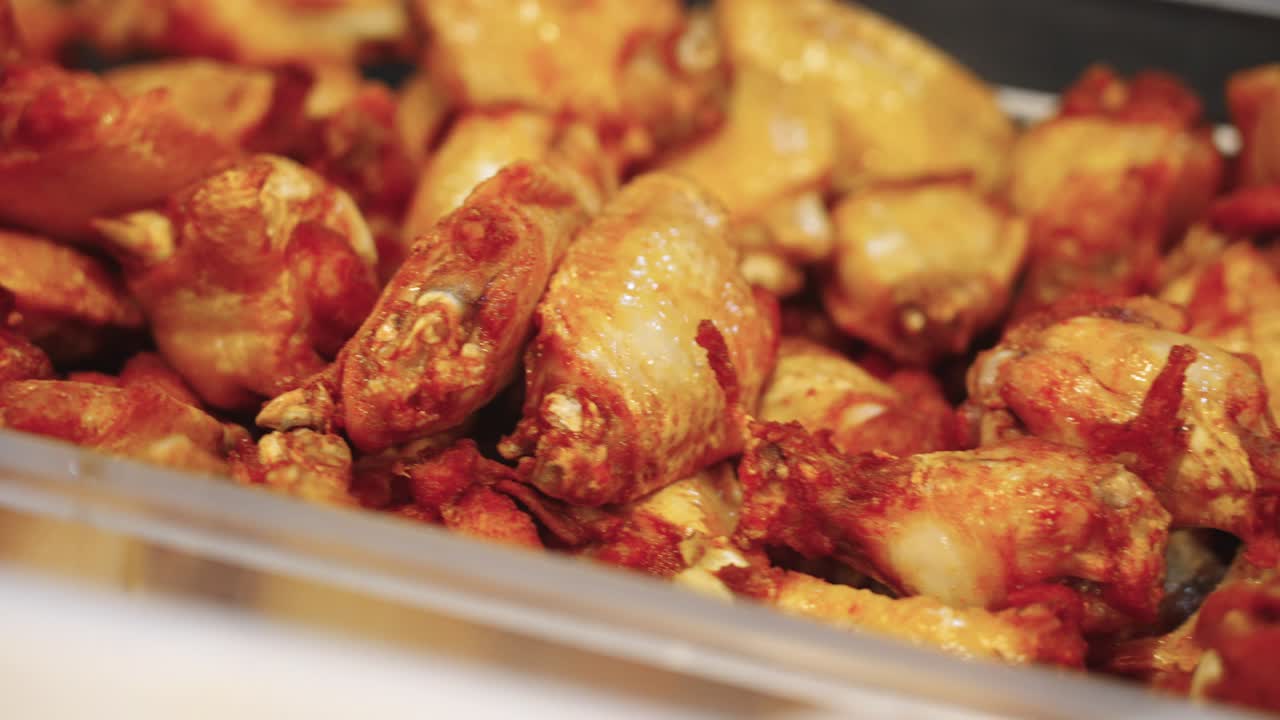 Riprese 4K ravvicinate con panoramica a destra di ali di pollo fresche appena uscite da una friggitrice, che mostrano una consistenza croccante e dorata, una superficie calda e saporita e una preparazione di cibo in cucina professionale.