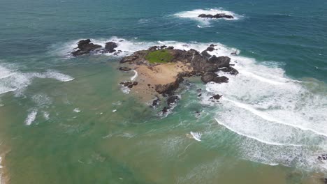drone towards rocky headland with white waves splash through rocks at sawtell beach near bonville peninsula in new south wales, australia